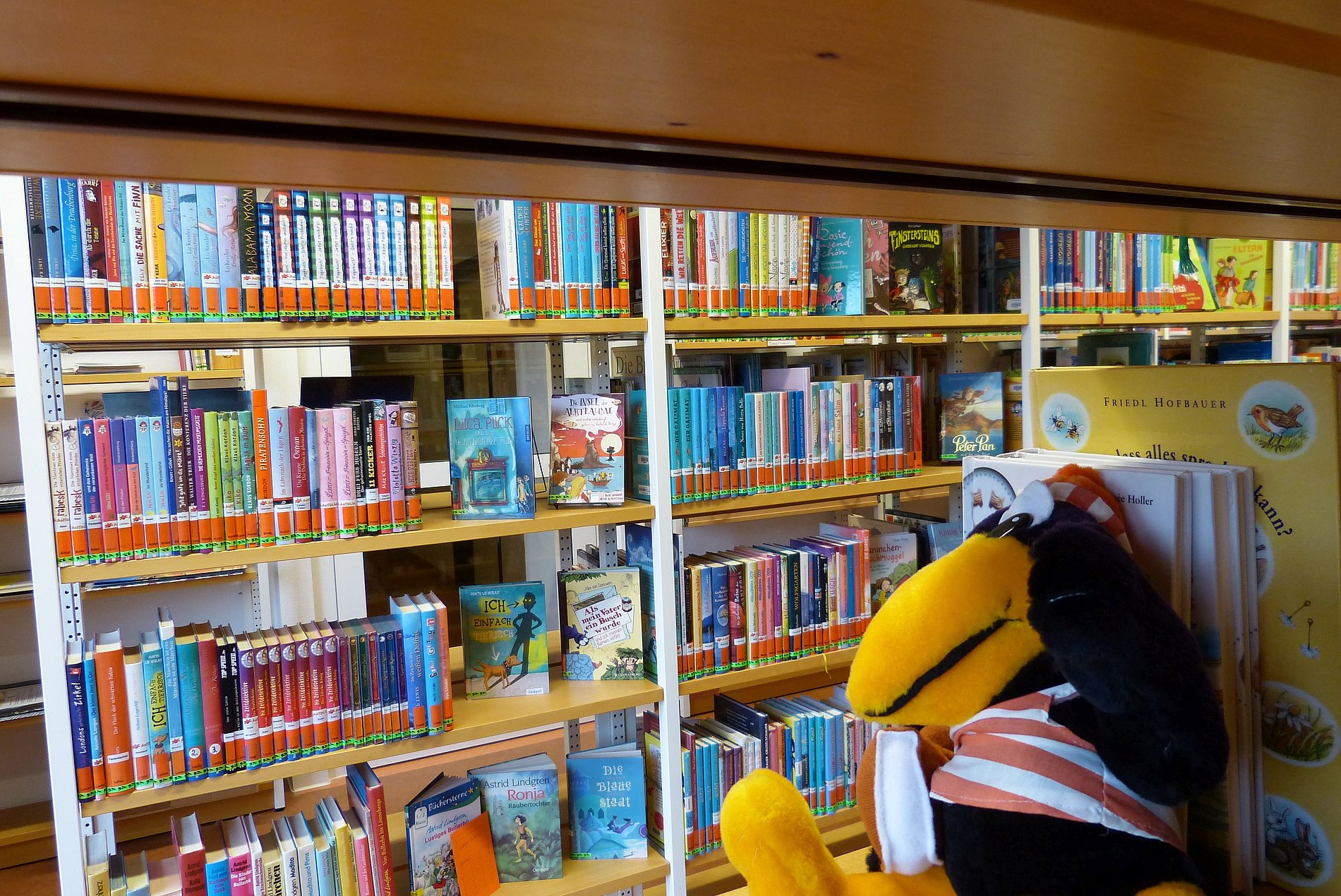 Blick in die Ergänzungsbücherei Der Marabu sitzt im Regal und schaut sich die Kinderbücher an.