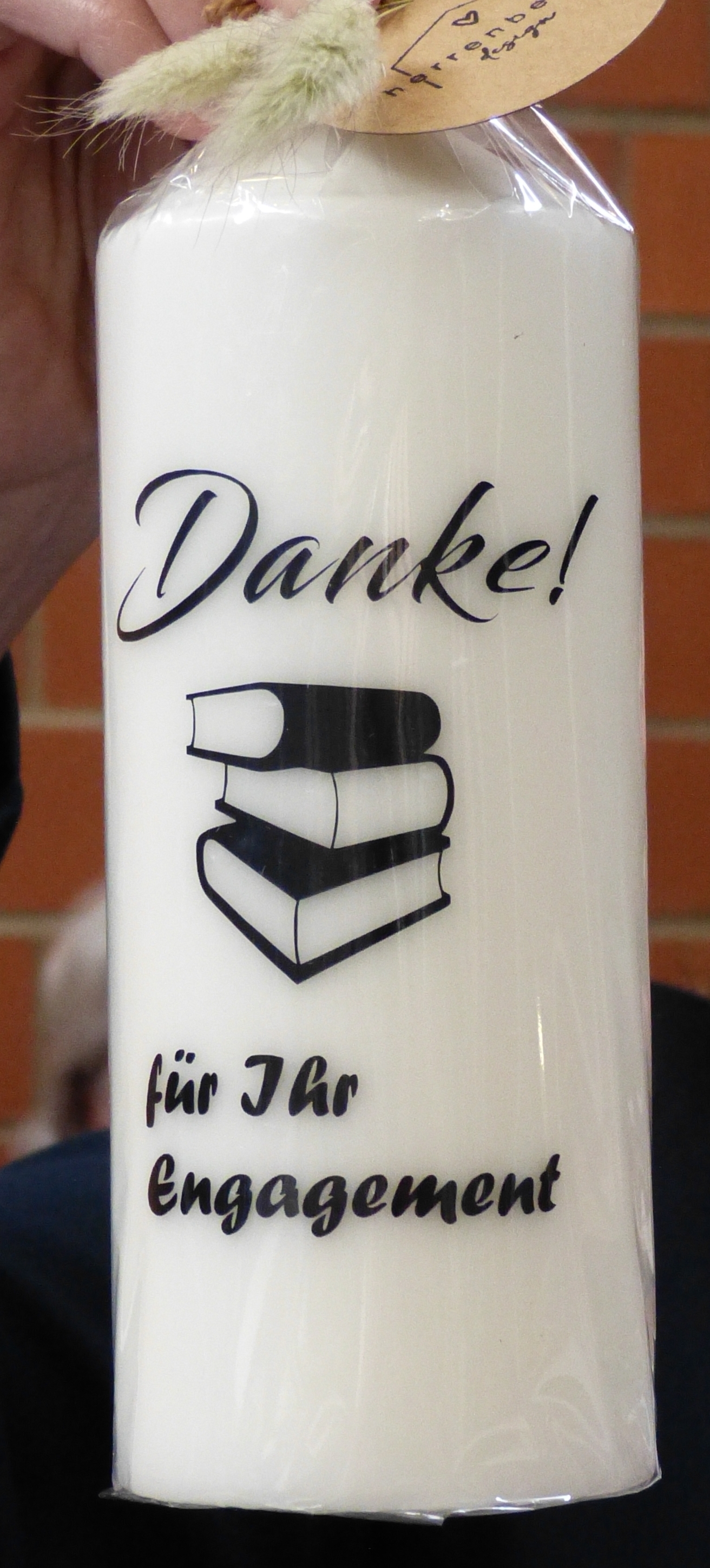 Kerze mit der Aufschrift "Danke für Ihr Engagement" mit einem Bücherstapel.